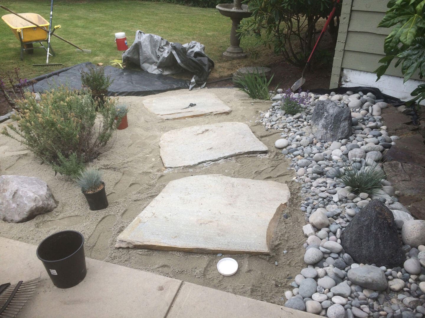 Stepping stones arranged on sand alongside a garden bed with rocks.
