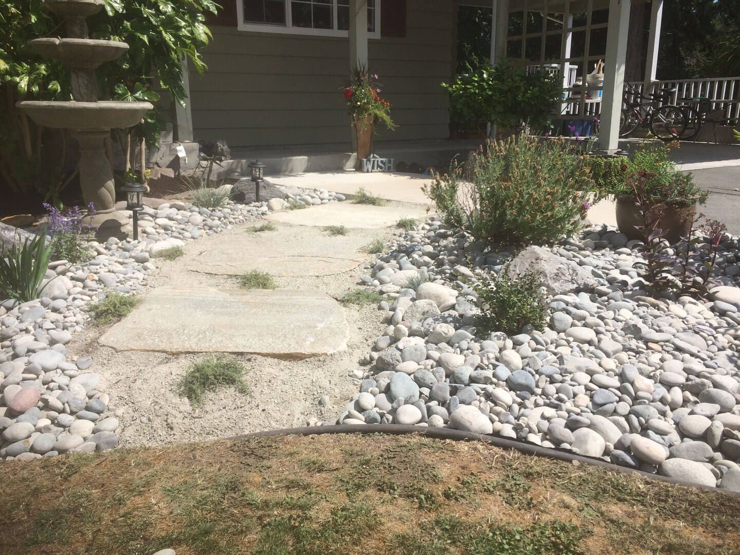 A stone pathway surrounded by white rocks and sparse greenery beside a house.