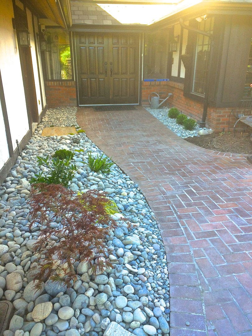 A brick pathway with rock and plant borders under natural light.