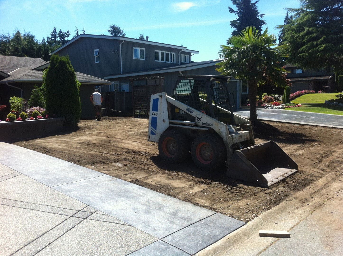 A skid steer loader working on a residential driveway.