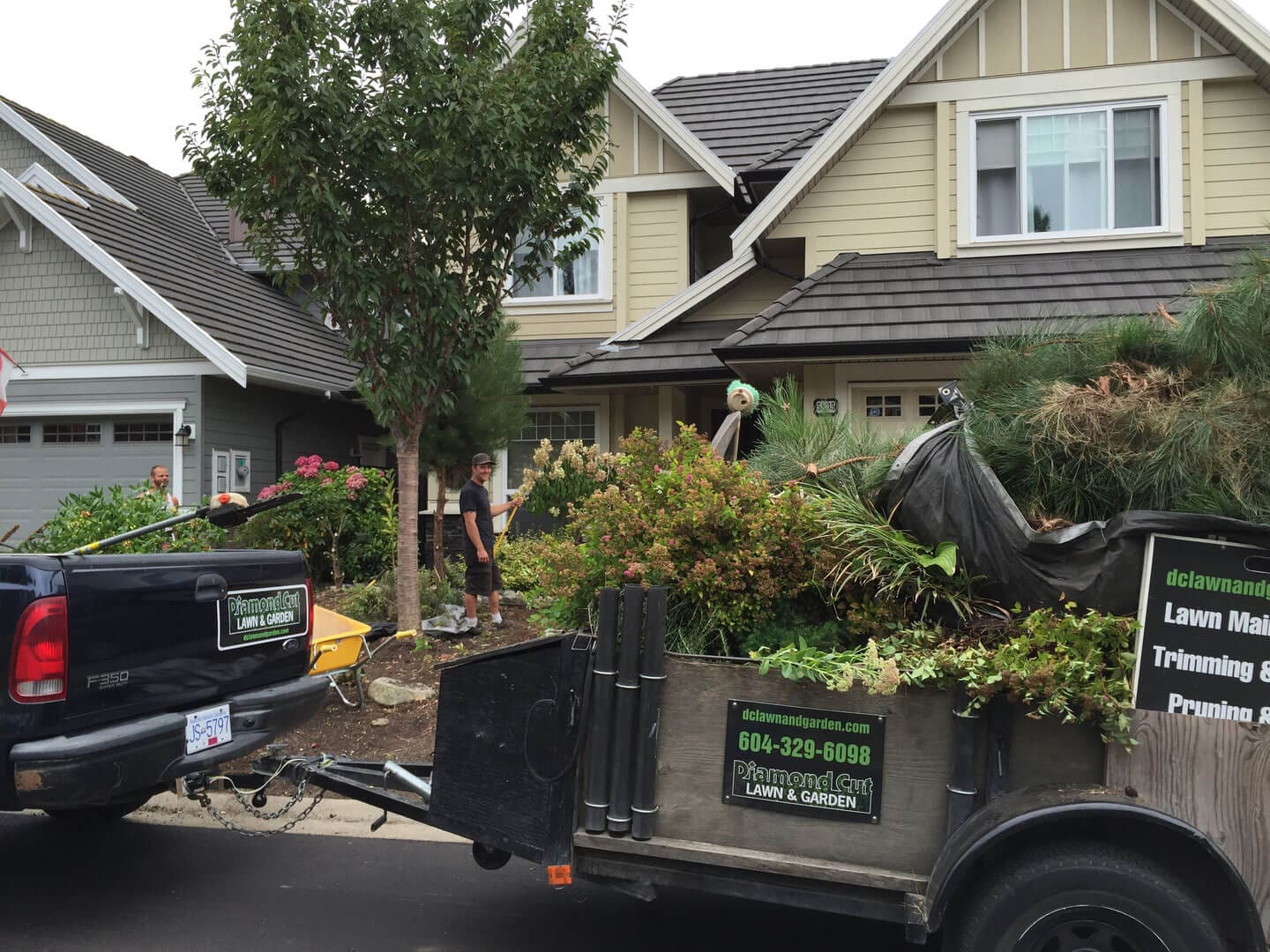 Truck and trailer loaded with garden waste parked in front of a house.