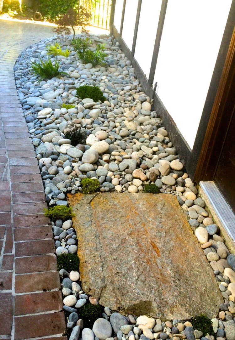 Stone path with pebbles and moss beside a building entrance.