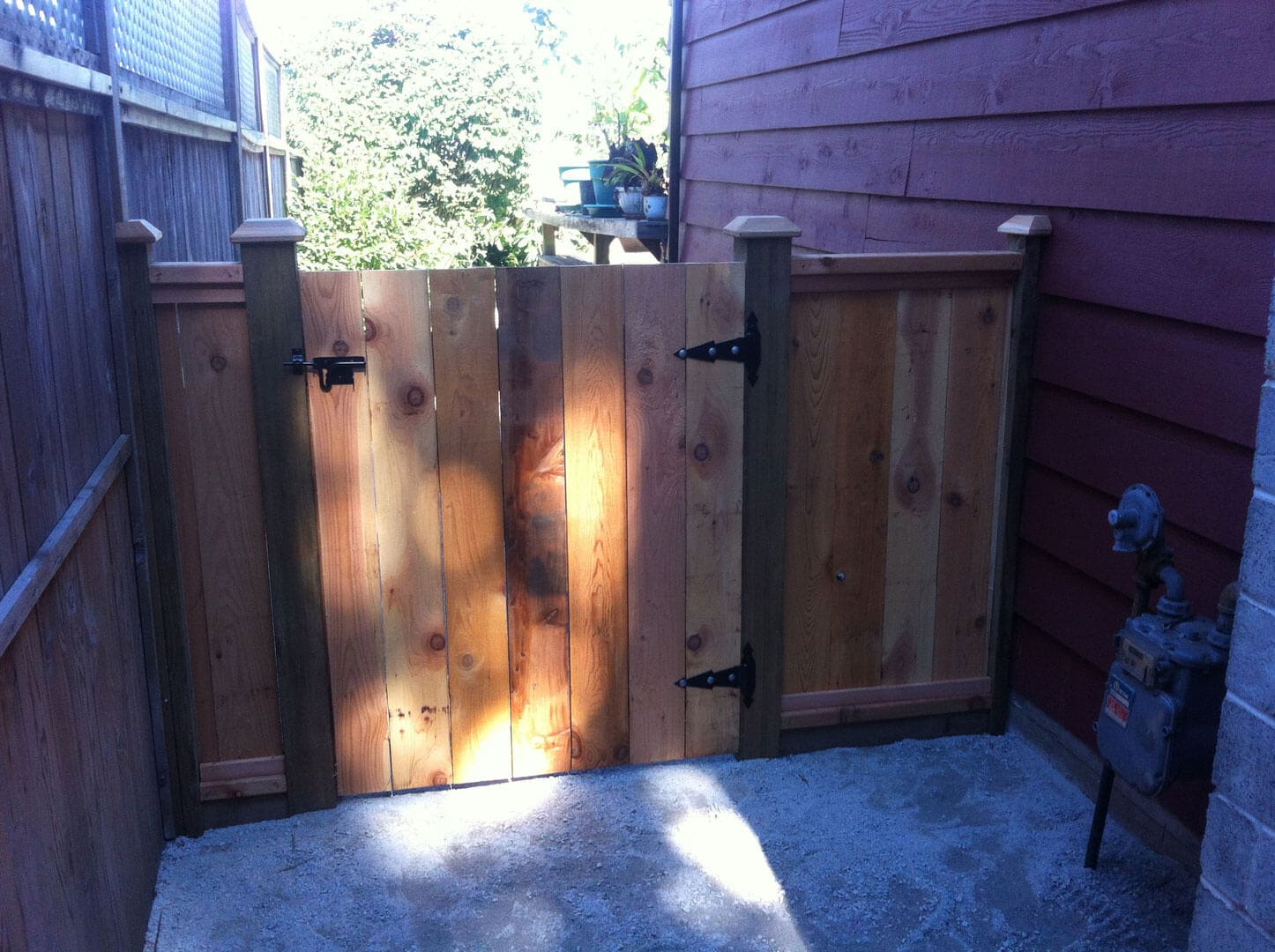 Wooden gate between two fences with sunlight casting shadows.