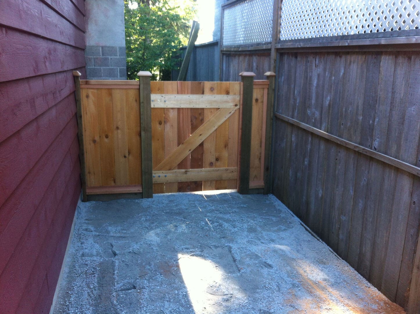 Wooden gate and fence enclosing a small backyard area with concrete floor.